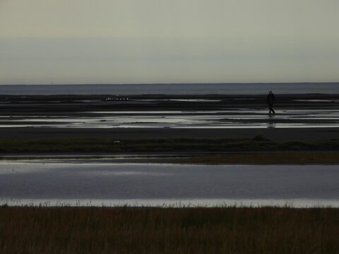 Un homme marche sur des terres humides près de Vesturhorn, en Islande, avec des reflets dans l'eau et un ciel nuageux.