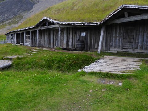 Bâtiment en bois avec un baril à Vesturhorn, Islande, entouré de verdure et de collines.