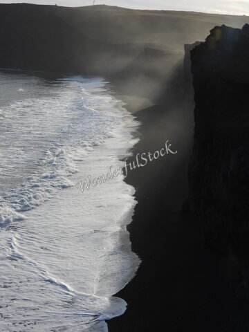 Plage de sable noir et falaises à Dyrhólaey, Islande, avec des vagues déferlant sur le rivage.