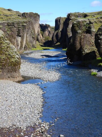 Fjaðrárgljúfur en Islande, canyon avec des parois rocheuses et une rivière serpentant au fond, entouré de verdure.