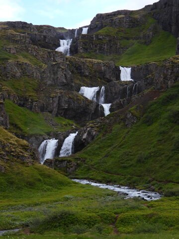 Chutes d'eau à Klifbrekku, Islande, entourées de collines verdoyantes et de rochers.