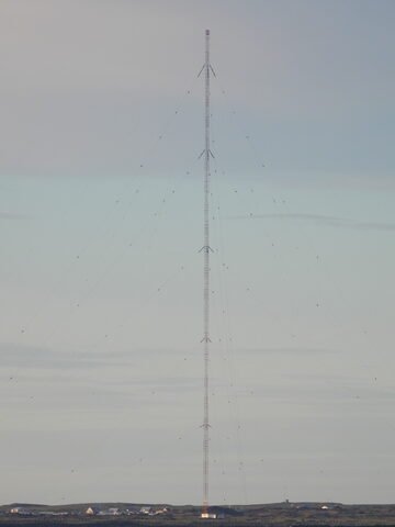Antenne de transmission à Öndverðarnes, Islande, avec des bâtiments en bas et un ciel nuageux en arrière-plan.