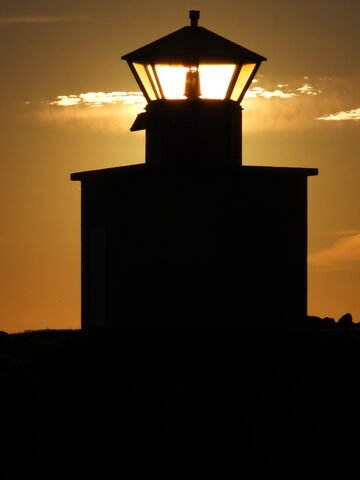 Phare silhouette à Öndverðarnes, Islande, illuminé par le soleil couchant, avec un ciel nuageux en arrière-plan.