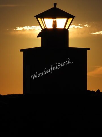 Phare silhouette à Öndverðarnes, Islande, illuminé par le soleil couchant, avec un ciel nuageux en arrière-plan.