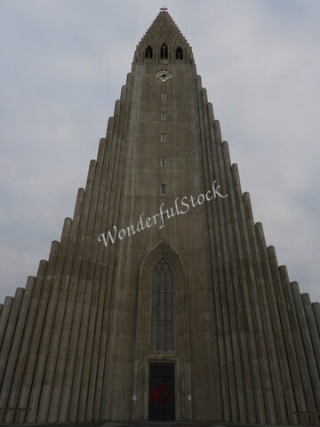 Église en béton à Reykjavik, Islande, avec une façade en forme de flèche et une horloge au sommet.
