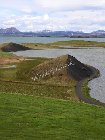 Paysage de collines verdoyantes et de plans d'eau à Skútustaðir, Islande, avec des montagnes en arrière-plan et un sentier serpentant.