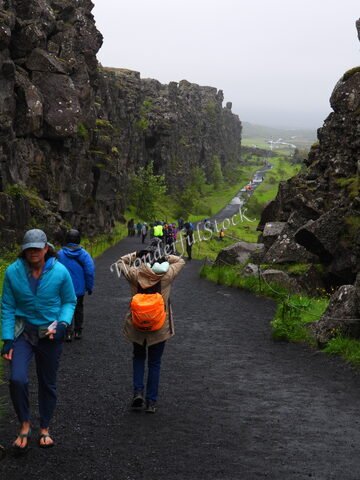 Sentier bordé de falaises à Thingvellir, Islande, avec des visiteurs marchant sous un ciel nuageux.