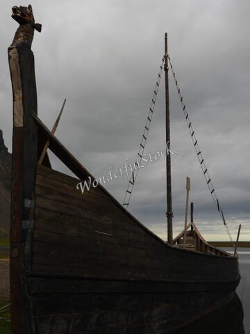 Un bateau viking en bois se tient près de Vestrahorn, en Islande, sous un ciel nuageux, avec une montagne en arrière-plan.