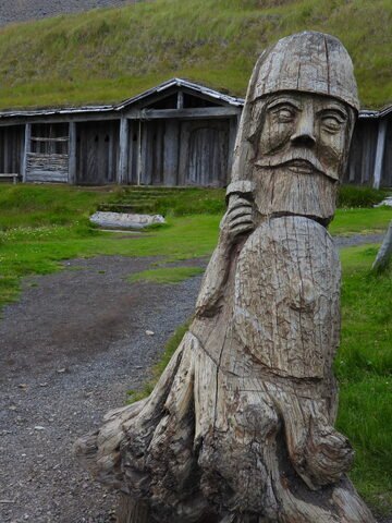 Sculpture en bois représentant un personnage, avec une maison en bois en arrière-plan, à Vestrahorn, Islande.