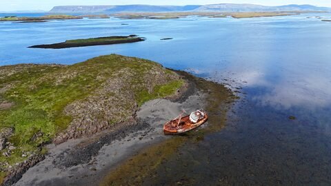 Un bateau échoué sur une plage rocheuse entourée d'eau et de paysages verdoyants en Islande.