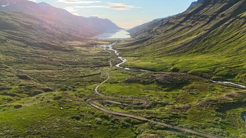 Vallée verdoyante avec une route sinueuse et un lac en Islande, Klifbrekku.