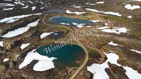 Lacs entourés de neige et de rochers à Klifbrekku, Islande, avec une route sinueuse traversant le paysage.