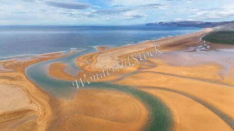 Rivière serpentant à Rauðisandur, Islande, avec des plages de sable doré et des eaux calmes sous un ciel nuageux.