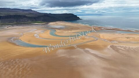Rivière serpentant à travers des plages de sable doré à Rauðisandur, Islande, avec des collines en arrière-plan et la mer au loin.