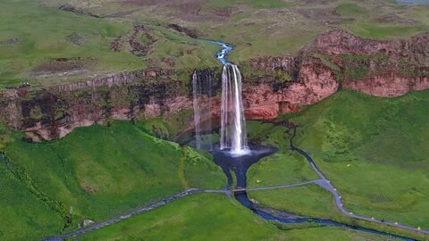 Chute d'eau Seljalandsfoss en Islande, entourée de paysages verdoyants et de formations rocheuses.