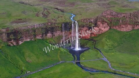 Chute d'eau Seljalandsfoss en Islande, entourée de paysages verdoyants et de formations rocheuses.