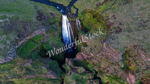 Cascade de Seljalandsfoss en Islande, entourée de végétation luxuriante et de formations rocheuses.