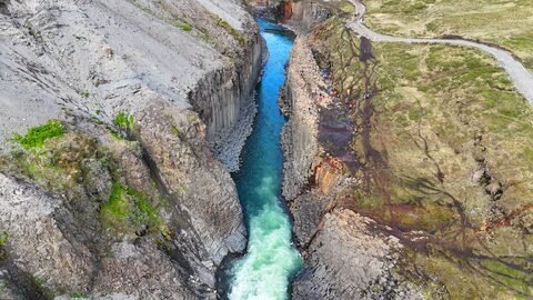Canyon de Stuðlagil en Islande, avec des parois rocheuses et une rivière turquoise au fond, entouré de verdure et de sentiers.