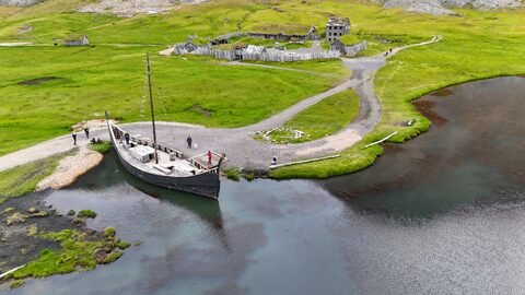 Un bateau en bois est amarré près d'une ancienne settlement à Vestrahorn, Islande, entouré de verdure et d'un lac.