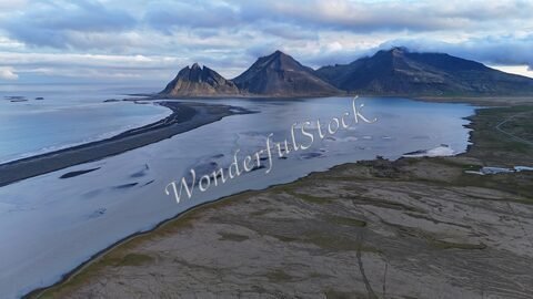 Vestrahorn en Islande, avec des montagnes abruptes et une plage de sable clair se prolongeant le long d'une mer calme.