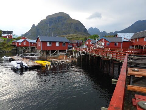 Maisons en bois rouge sur pilotis au bord de l'eau, entourées de montagnes, en Norvège.