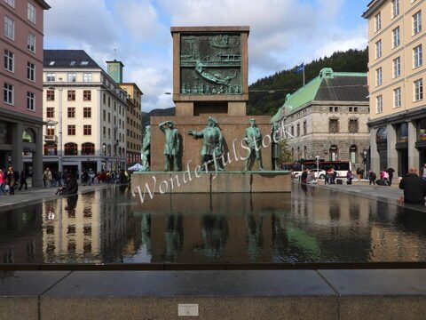 Statue de marins au centre de Bergen, Norvège, avec des bâtiments colorés et des montagnes en arrière-plan.