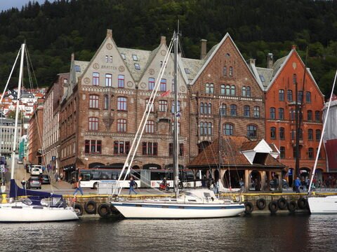 Bateaux amarrés près des maisons en briques à Bergen, Norvège, avec des collines verdoyantes en arrière-plan.