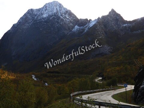 Montagnes enneigées et route sinueuse à Bergsbotn, Norvège, entourées de végétation automnale et d'un ruisseau.