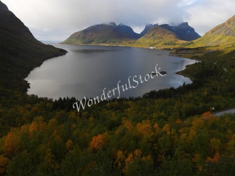 Lac entouré de collines et de montagnes à Bergsbotn, Norvège, avec des arbres aux couleurs automnales.