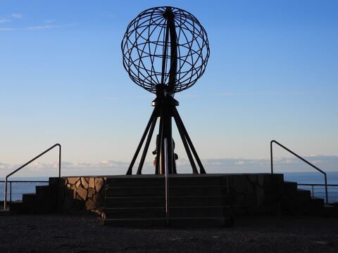 Globe terrestre au Cap Nord, Norvège, avec un ciel dégagé et des escaliers en pierre menant à la plateforme d'observation.