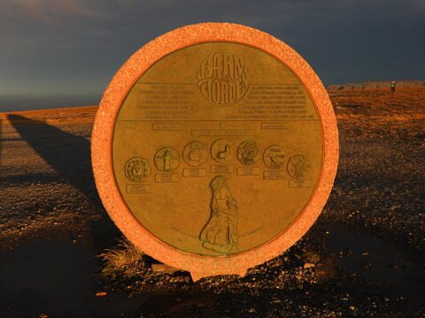 Panneau commémoratif au Cap Nord, Norvège, avec des symboles et une silhouette humaine en arrière-plan.