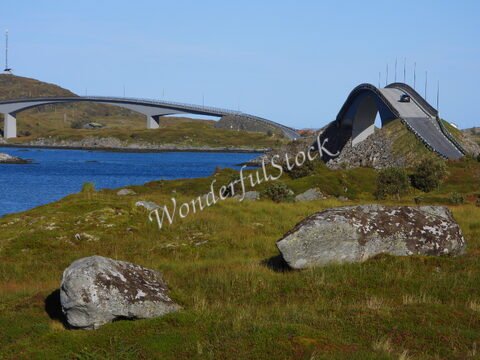 Pont sur l'eau à Flakstad, Norvège, entouré de rochers et de verdure.