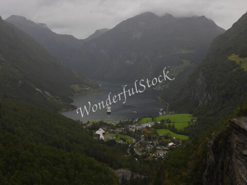 Vue panoramique de Flydalsjuvet en Norvège, avec des montagnes verdoyantes et un fjord où navigue un bateau.