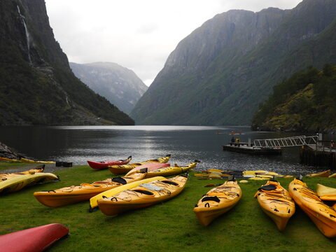 Des kayaks jaunes sur une pelouse au bord de l'eau à Gudvangen, Norvège, avec des montagnes en arrière-plan.