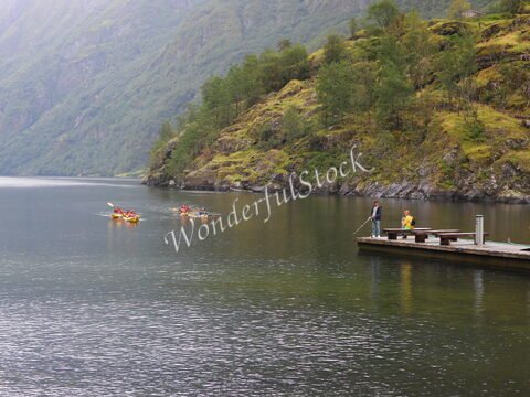 Des kayaks naviguent sur un fjord à Gudvangen, en Norvège, avec des collines verdoyantes en arrière-plan.