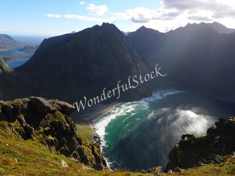 Plage de Kvalvika en Norvège, entourée de montagnes avec des vagues vertes et des rochers au premier plan.