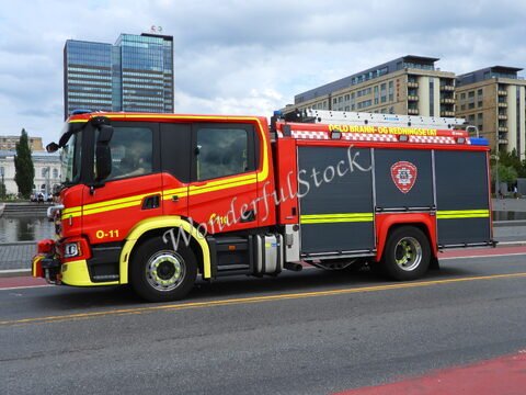 Camion de pompier rouge à Oslo, Norvège, avec des bâtiments modernes en arrière-plan et un reflet dans l'eau.