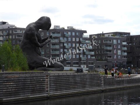 Statue assise à Oslo, Norvège, entourée de bâtiments modernes et d'un quai le long de l'eau.