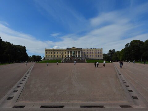 Palais royal à Oslo, Norvège, avec des visiteurs sur l'esplanade et un ciel partiellement nuageux.