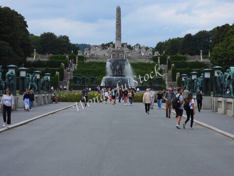 Foule se déplaçant vers une fontaine au parc de sculptures à Oslo, Norvège, avec des statues et des jardins verdoyants en arrière-plan.