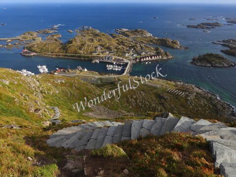 Vue plongeante sur le port de Reinebringen en Norvège, avec des maisons colorées et des bateaux amarrés dans une baie entourée d'îles.