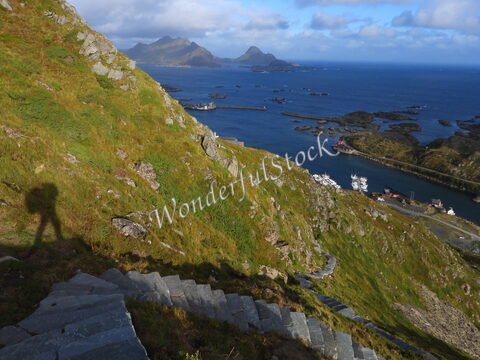 Vue sur un sentier escarpé et verdoyant à Reinebringen, Norvège, avec des îlots et des bateaux dans la mer.