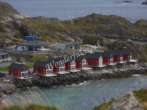 Maisons sur pilotis rouges au bord de l'eau à Reinebringen, Norvège, avec des collines et des rochers environnants.
