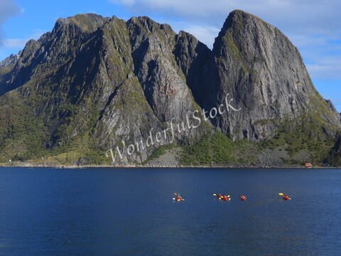 Des kayakistes naviguent dans les eaux de Sakrisøy, en Norvège, avec des montagnes escarpées en arrière-plan.