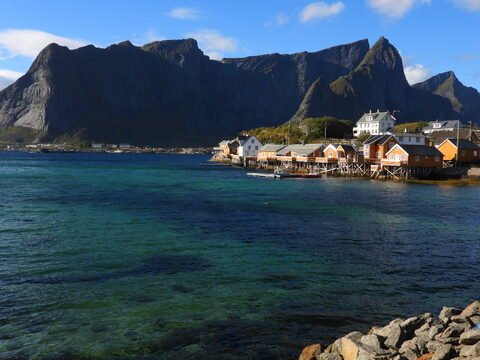 Maisons de pêcheurs colorées sur pilotis à Sakrisøy, Norvège, avec des montagnes en arrière-plan et une mer turquoise.