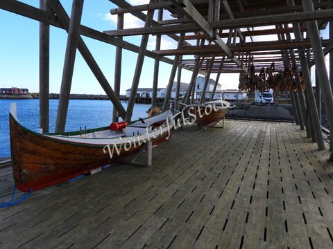 Bateaux en bois sur un quai à Sakrisøy, Norvège, avec des cabanes et du poisson séché suspendu au-dessus.