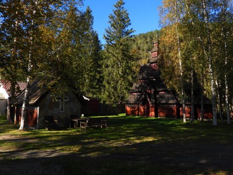 Église en bois de style stavkirke à Savjord, Norvège, entourée d'arbres et de bancs en bois.