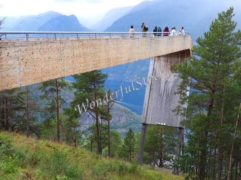 Plateforme d'observation en bois à Stegastein, Norvège, avec des visiteurs admirant les montagnes et le fjord en contrebas.