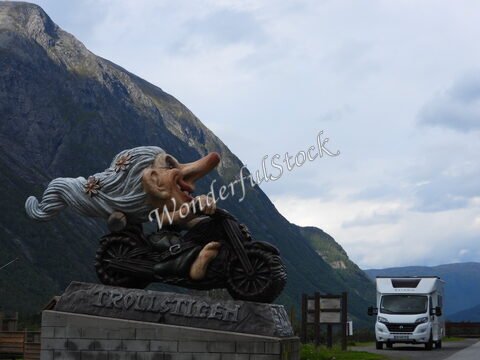 Sculpture d'un troll sur une moto à Trollstigen, Norvège, avec des montagnes en arrière-plan et un camping-car.