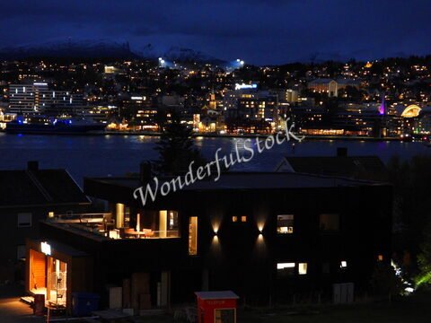 Vue nocturne de Tromsø, Norvège, avec des bâtiments illuminés et des montagnes en arrière-plan.